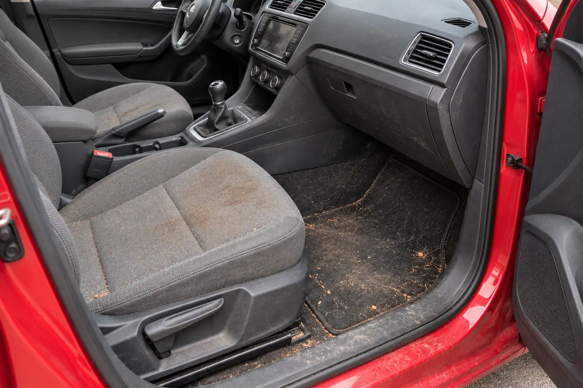 Interior de un coche con suciedad acumulada: tierra y barro seco en el asiento, la moqueta, la alfombrilla y el salpicadero