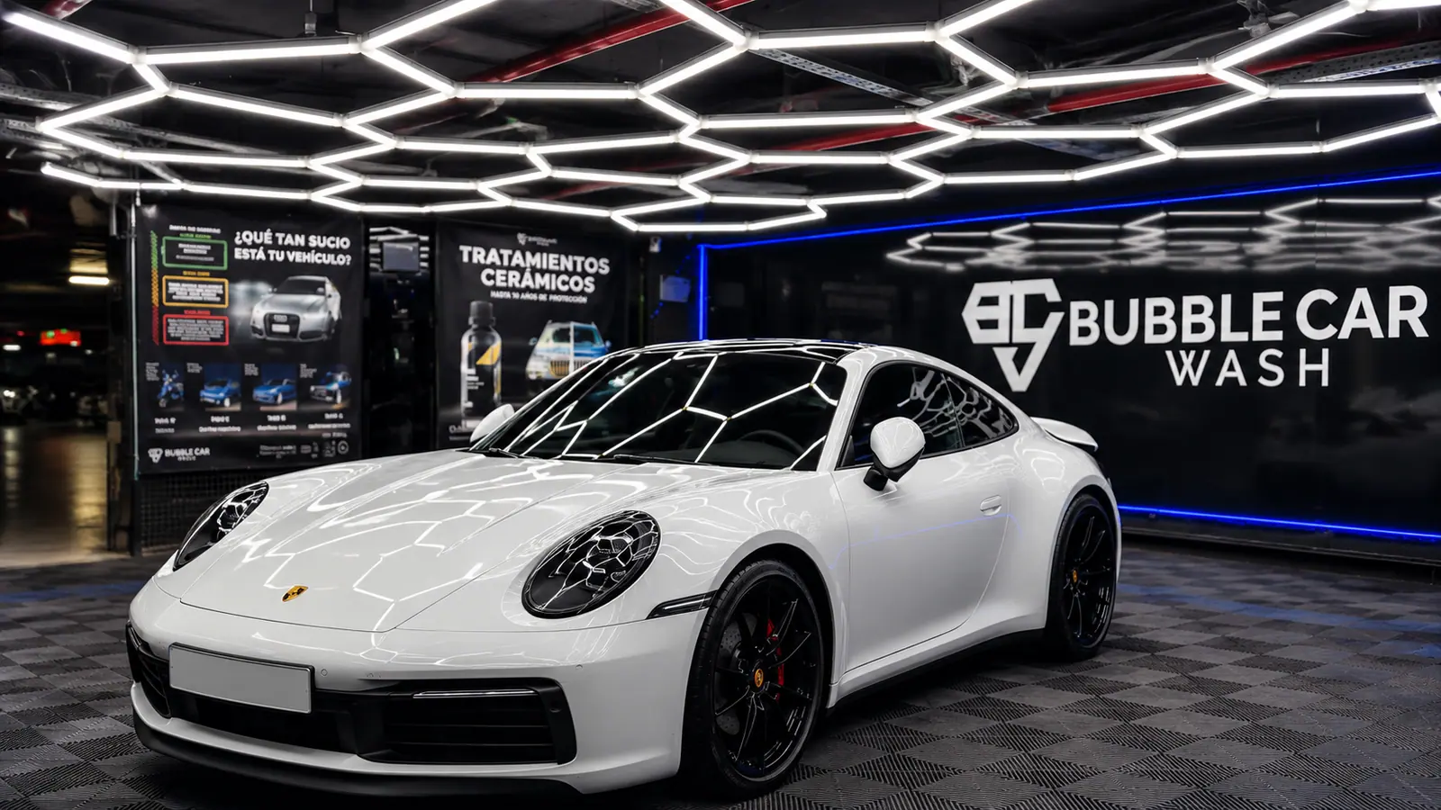Centro Bubble Car Wash Serranopark 1: coche blanco deportivo bajo luces hexagonales, con el rótulo Bubble Car Wash y carteles de la escala de suciedad y de tratamientos cerámicos al fondo